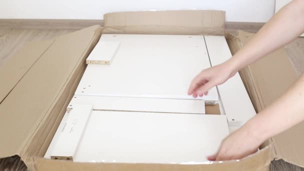 Чоловік розпаковує шматок меблів з картону, працюючи — стокове відео