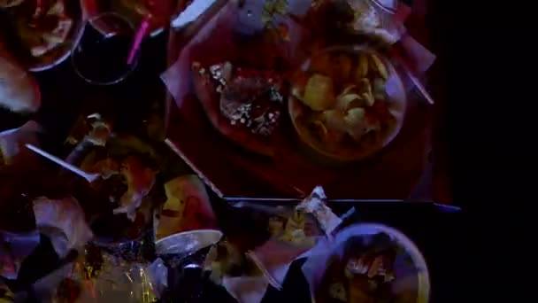 Špatné jídlo rychlé občerstvení a hranolky, zbytky jsou na stole, blikání z televizní obrazovky, pozadí — Stock video