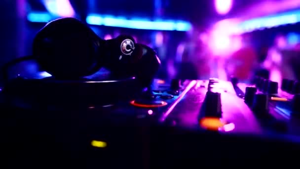 DJ-Musik-Bedienfeld mit Kopfhörern auf dem Hintergrund tanzender Menschen in einem Nachtclub, Kopierraum — Stockvideo