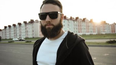 Vahşi stil sahibi bir adam gün batımında kameraya bakar. Siyah gözlüklü, modaya uygun, sakallı adamın portresi. Küpeli modaya uygun biri ağır çekimde duruyor. Sabit çekim