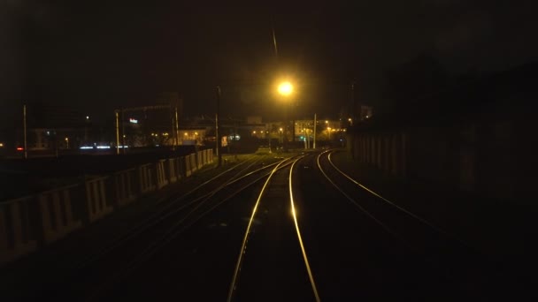 Kilátás az utolsó vasúti kocsi hátsó ablakából mozgó sínekre éjszaka. Utazási és turisztikai koncepció. Vasúti személyvonat halad át a városon. A vörös szemafor fénye ragyog. — Stock videók