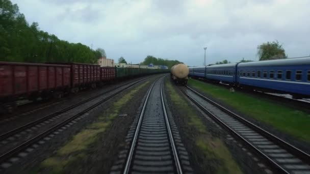 Railway train goes between freight cargo wagons outside of town. View on rails in motion from rear back window of last railroad coach carriage. Export import concept. — Stock Video