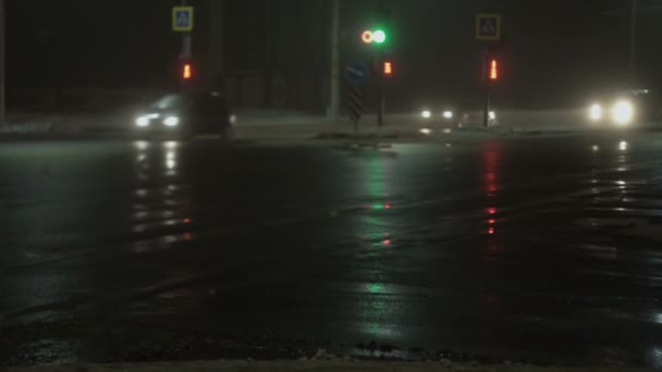 Αυτοκίνητα, οχήματα περνούν από το σταυροδρόμι με φανάρια. Νυχτερινή πόλη σε ομίχλη το χειμώνα. Αργή κίνηση. Αντανάκλαση σε υγρή άσφαλτο. Φως από προβολείς. Κακή ορατότητα για οδική κυκλοφορία, κακοκαιρία — Αρχείο Βίντεο