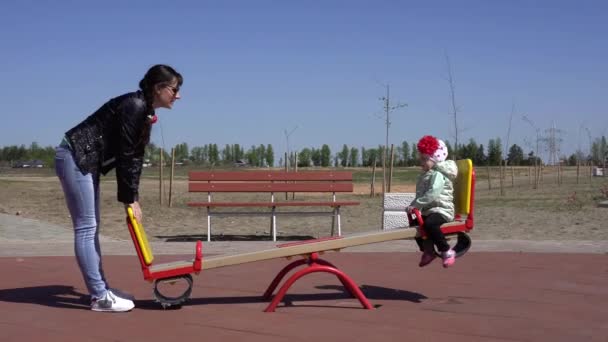 Pequena menina bonita brinca em um parque infantil moderno com sua mãe. Tempo de primavera ensolarado, novo playground com slides e balanços, feliz — Vídeo de Stock