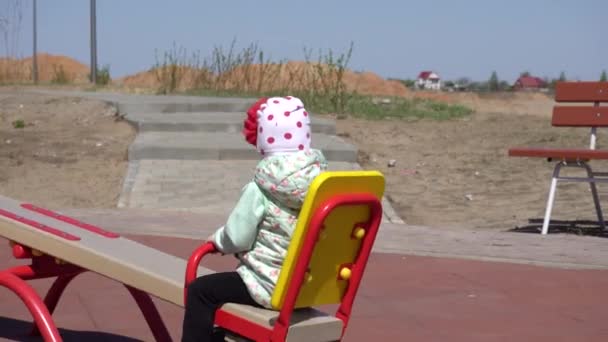 Gyönyörű kislány 2 éves lovagol a hintán a játszótéren, boldog — Stock videók