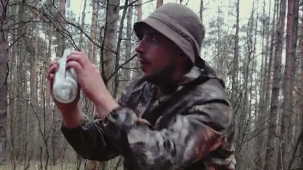 Alcoholic drinker concept. Hunter forest ranger is holding an empty bottle and says something. Strange man dressed in camouflage suit with mustache, stubble in panama hat. Funny comical situation — Stock Video