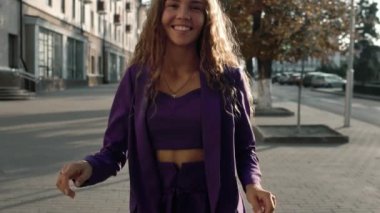 Şehir sokağında dans eden uzun kıvırcık saçlı mutlu kız. Takım elbiseli şık iş kadını ağır çekimde hareket ediyor. Pozitif kavram. Vogue dişisi kameraya bakar. Moda modeli