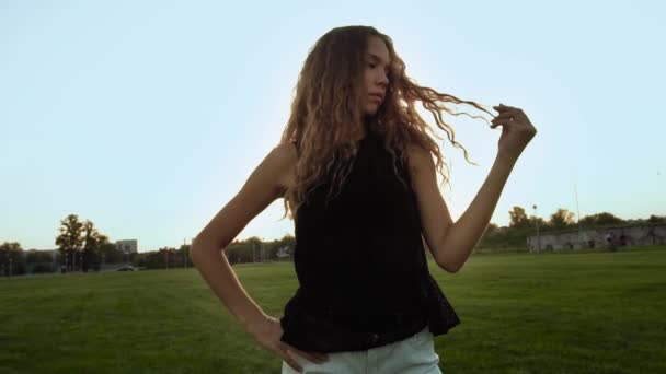 Modelo femenina de Vogue posando afuera. Retrato de chica seria de pelo largo rizado caucásico sin maquillaje. Puesta de sol. La mujer a la moda de estilo mira en la cámara, se detiene en cámara lenta bajo los rayos del sol — Vídeo de stock