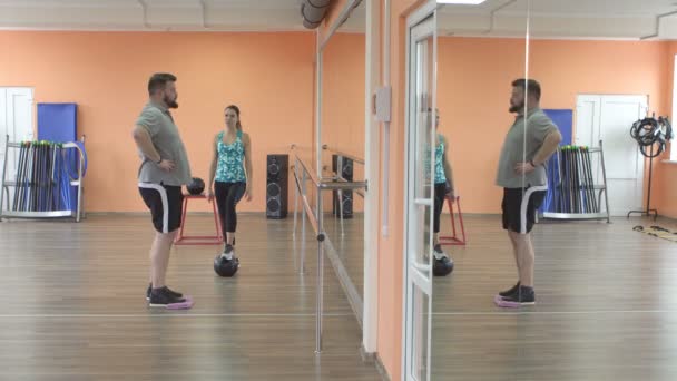 Een jonge blanke meisjestrainer traint een man met een baard in een fitnessruimte voor het verbranden van vet. Problemen met overgewicht, gezondheid — Stockvideo