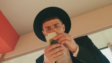 Siyah takım elbiseli ve şapkalı adam Yahudi ya da İtalyan mafyasına benziyor. Düşük açı, alt görüş. İnsan akıllı telefon ekranına bakar ve kendi ilişkilerine karar verir. Sakallı ve bıyıklı bir iş adamı.