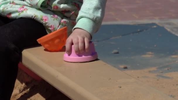 Klein mooi meisje van 2 jaar oud speelt in de zandbak met speelgoed op de speelplaats, close-up, Kaukasisch — Stockvideo