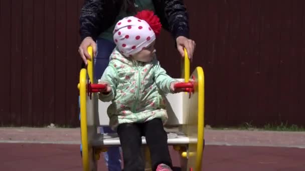 En liten vacker kaukasisk flicka leker på lekplatsen med sin mamma. solig våren väder bakgrund — Stockvideo