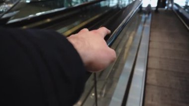Tıbbi koruyucu eldiveni olmayan kol, alışveriş merkezinde yürüyen merdivene binerken tırabzanlara tutunur. Coronavirus. Seyahat konsepti. Adam metrodan, havaalanından, tren istasyonundan yukarı çıkıyor.