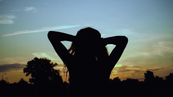 Dziewczyna rzuca długie włosy rękami w sylwetkę o zachodzie słońca w zwolnionym tempie, ciemna postać. Pojęcie wolności, przyjemności, wakacji, odpoczynku. Zaparkuj na zewnątrz. Zbliżenie. Stabilny strzał — Wideo stockowe