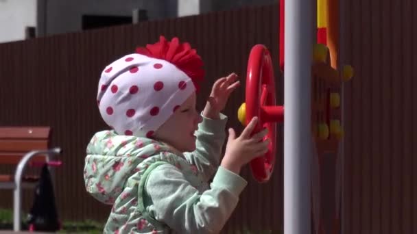 En vacker liten flicka leker på en modern lekplats med sin mamma. Soligt vårväder, ny lekplats med rutschbanor och gungor, glad — Stockvideo