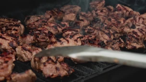 El cocinero prepara carne fresca en la parrilla, voltea la carne para freír uniformemente. La carne apetitosa jugosa es barbacoa, mo lento, carne a la parrilla — Vídeo de stock