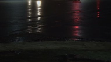 Kamyon kavşağı ve caddeyi geçiyor. Kışın sisli bir gece şehri. Tekerleklerin yakın görüntüsü. Islak asfalta yansıyor. Farlardan gelen ışık.