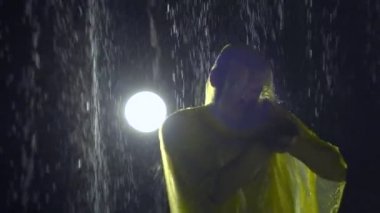 Yağmurda yağmurluk giymiş bir adam süpürgeden ateş eder, bir skeç prova eder. Stüdyo fotoğrafçılığı, arkaplan, yavaş çekim