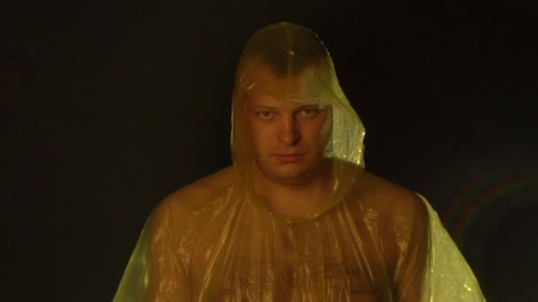 Мокрый кавказский мужчина в плаще смотрит на камеру на черном фоне, копирует пространство — стоковое видео