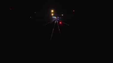 Tren gece şehri terk ediyor. Son vagon vagonunun arka camından hareket halindeki raylara bakın. Seyahat ve turizm konsepti. Demiryolu yolcu treni. Kırmızı semafor ışığı parlıyor.