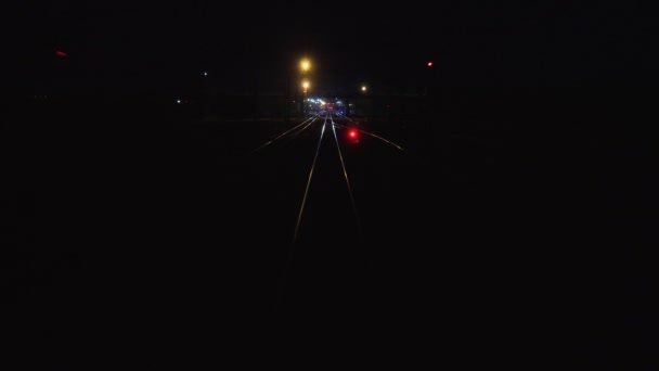 O comboio sai da cidade à noite. Vista sobre carris em movimento a partir da janela traseira da última carruagem de carruagem ferroviária. Viagens e turismo conceito. Comboio ferroviário de passageiros. semáforo vermelho luz está brilhando — Vídeo de Stock