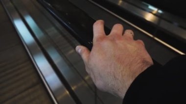 Tıbbi koruyucu eldiveni olmayan el alışveriş merkezindeki merdiven korkuluğuna tutunuyor. Seyahat konsepti. Coronavirus. Kapatın. Adam metroya, havaalanına, tren istasyonuna gidiyor.