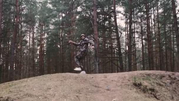 Chasseur étrange homme habillé en costume de camouflage danse techno. Un garde forestier de 30 ans qui s'amuse. Blogueur caucasien avec moustache et chaume en panama chapeau et baskets saute et secoue son corps — Video