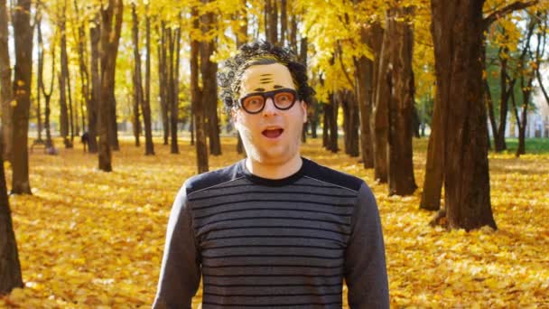 A young guy in a wacky mask on his face rejoices in autumn and looks at the camera, emotion — Stock Video