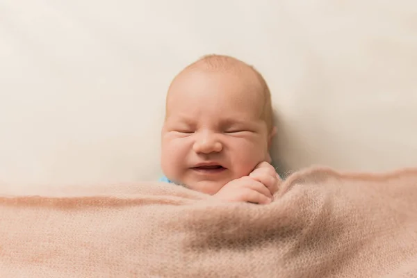 Yeni doğmuş bebek yüzünü buruşturuyor. Bej arkaplanda duygusal bir bebek