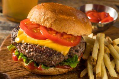 Ev yapımı Grass Fed Cheeseburger, yanında patates kızartması ve bira.