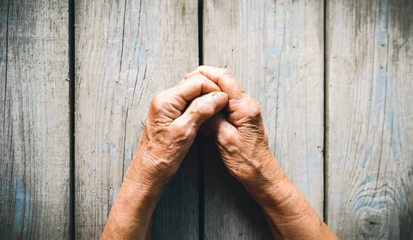 Elderly woman hands on rustic wooden background. Senior woman with fingers crossed. Wrinkled palms stretched forward. Religion, take care, mothers day, warmth concept. Human emotions, old people health, love and compassion.