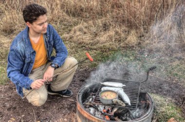 Genç bir adam üzerinde bir kamp ateşi Minnesota sosisli sandviç, Mısır ve çorba aşçılar