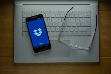 Dropbox app loading on Android phone in a dark room clipart
