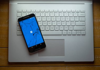 Bir lapto üzerinde oturan yükleme Facebook app ile kırık bir telefon