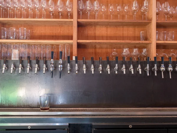 Row of beer taps in back of bar with glasses on shelf — Stock Photo, Image