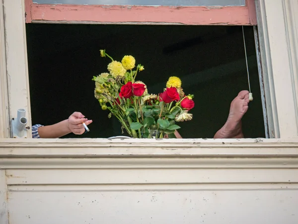 Flores, pies y cigarrillos colgando de una ventana — Foto de Stock