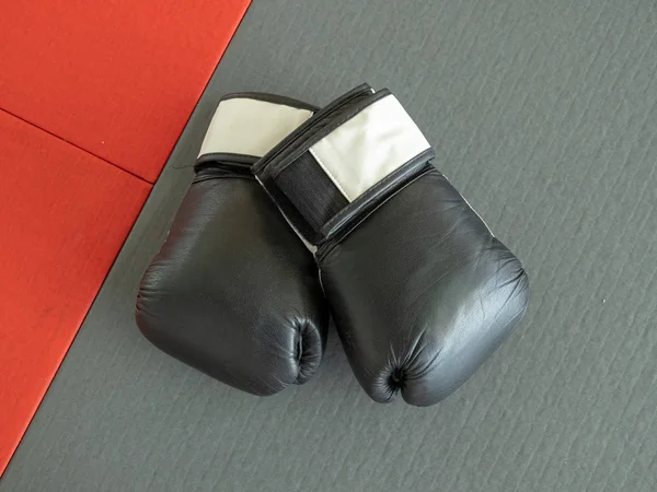 Overhead view of black boxing gloves sitting on mats of boxing gym