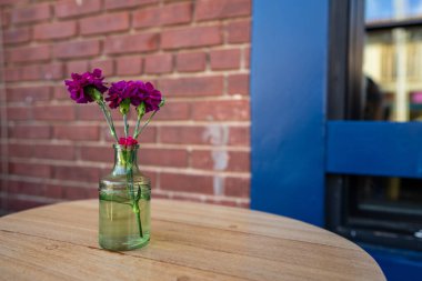 Açık hava masasında cam vazoda duran mor karanfil çiçeği.