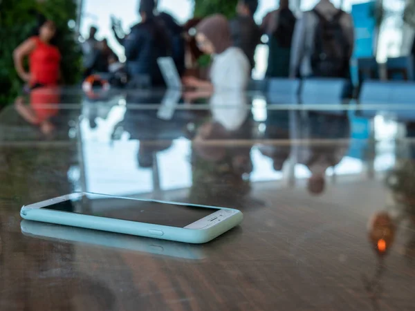 Teléfono celular con estuche envejecido descansando en la mesa de una tienda ocupada — Foto de Stock