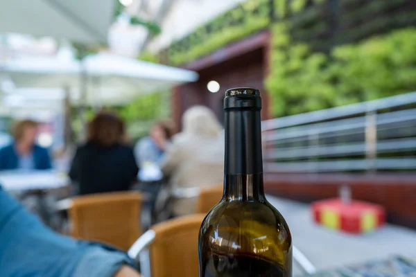 Open bottle of red wine at an outdoor restaurant with patrons