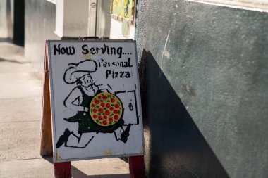 Şimdi kaldırımdaki pizzacının önünde pizza tabelaları servis ediliyor.