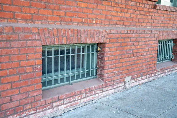Window grade blocking lower floors of a brick warehouse building on sidewalk — 스톡 사진