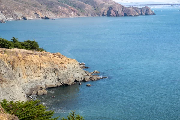 Acantilado rocoso en el cuerpo de agua con excursionistas y puente en el fondo — Foto de Stock