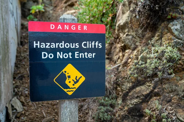 Danger hazardous cliffs do not enter with person falling sign on wooden post leading up hill