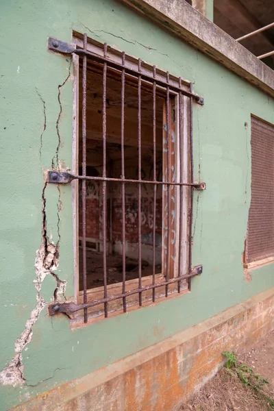 Puerta de acero oxidado que bloquea la ventana en un edificio en ruinas con hormigón cayendo a pedazos — Foto de Stock