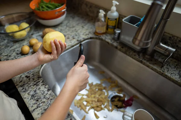 Kadın elleri akşam yemeği için taraf tutarken patatesi lavaboya atıyor.