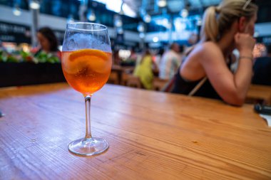 Orange cocktail in wine glass sitting on table at restaurant with woman in back