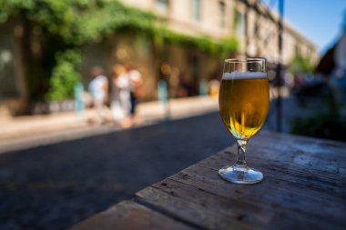 Full beer glass sitting on wooden picnic table in urban area in summertime