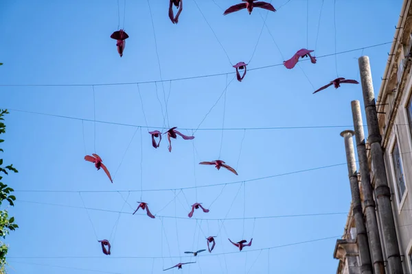 Pássaros de papel decorativos pendurados em cordas altas em edifícios contra o céu — Fotografia de Stock