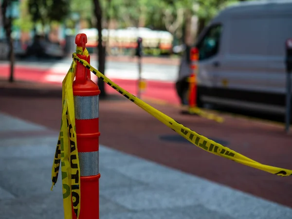 Cinta amarilla de precaución atada al cono de seguridad naranja en la acera con furgoneta en el fondo — Foto de Stock